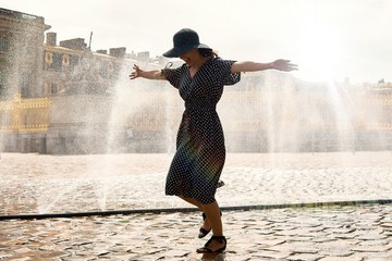 Happy girl in dress and hat in a spray of water on a sunny summer day, Versailles, France