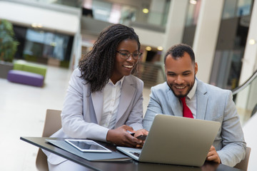 Smiling coworkers using laptop. Cheerful young African American business people sitting at table and using digital devices. Technology concept