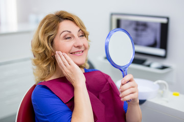 cheerful mature woman looking at her teeth in dental clinic