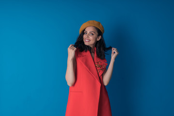 Naklejka premium Portrait of a happy girl in a stylish beret and red vest, like a Frenchwoman on a blue background