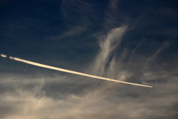 Contrails from an airplane descending through clouds in the sky