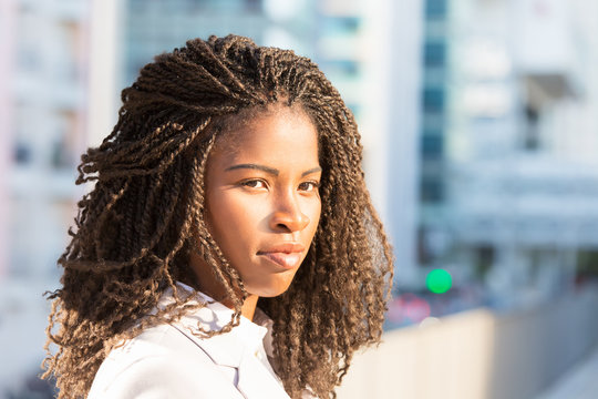 Pensive beautiful student girl posing in city. Closeup of young African American woman with dreads standing outside and looking at camera. Female portrait concept