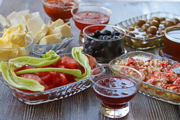 Breakfast with cheese, tomatoes, olives, butter and jam on wooden table.