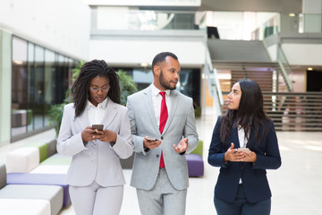 Business group with cellphones discussing project on their way to office. Business man and woman walking through office lobby and using smartphones. Mobile phones in business concept