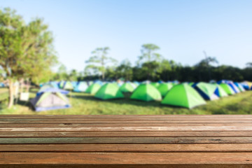 Old empty wood table top and blur of camping and tents in forest.