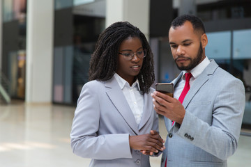 Focused businessman and businesswoman with smartphone. Confident young African American business people standing together and using mobile phone. Technology concept