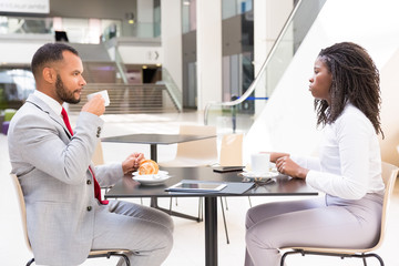 Diverse partners or colleagues meeting over cup of coffee. Side of business man and woman sitting at table in cafe, drinking coffee and talking. Business meeting or coffee hour concept