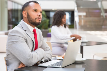 Pensive businessman thinking over new strategy over cup of coffee. Young black woman drinking coffee in background. Workspace concept