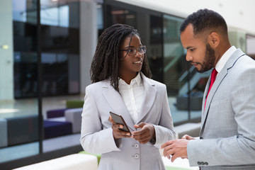Excited business colleagues watching content on mobile phone together. Business woman showing smartphone screen to male colleague. Media content concept