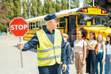 Group of children going out the school bus ready to cross the road while driver holding stop sign...