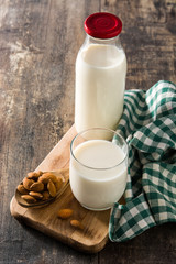 Almond milk in glass and bottle on wooden table.