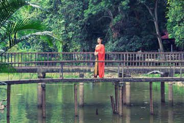 Thai woman in traditional dress standing on wooden bridge on lake with trees nature background