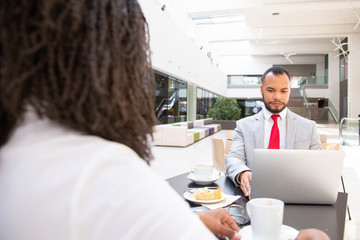 Business partners meeting at breakfast. Business man sitting at table with laptop, his female colleague drinking coffee. Corporate breakfast concept