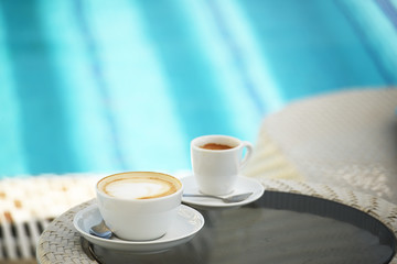 A cup of cappuccino and coffee on the background of emerald pool water.