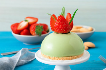 Blue wooden table with no-bake strawberry mini sphere matcha cheesecake with bowl of salt caramel, buiscuits and fresh strawberries, glass pitches and glass of milk.