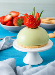 Blue wooden table with no-bake strawberry mini sphere matcha cheesecake with bowl of salt caramel, buiscuits and fresh strawberries, glass pitches and glass of milk.