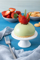 Blue wooden table with no-bake strawberry mini sphere matcha cheesecake with bowl of salt caramel, buiscuits and fresh strawberries, glass pitches and glass of milk.