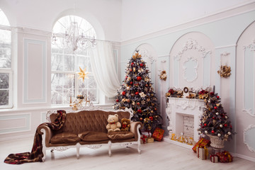Tall Christmas tree decorated with red ornaments, baroque sofa, stucco wall in spacious light room in baroque style.