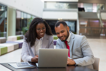 Smiling business colleagues using laptop. Cheerful young African American business people sitting at table and using digital devices. Technology concept
