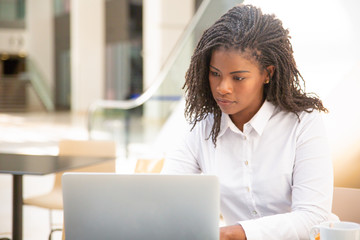 Focused female employee working in cafe. African American business woman using laptop in public space. Wireless technology concept