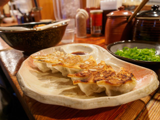 Wide closeup of a plate of Yaki Gyoza fried dumpling with a bowl of Ramen noodles on a restauraunt counter. Nakano, Tokyo, Japan. Travel and cuisine. - 289519055