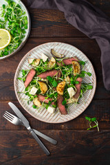 Green salad with steak, aubergine, sunflower sprouds and feta chese in ceramic plate on wooden background