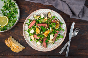 Green salad with steak, aubergine, sunflower sprouds and feta chese in ceramic plate on wooden background