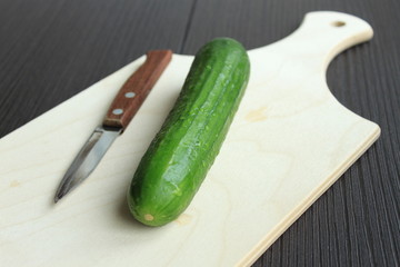 Cucumber and knife lie on a white wooden board.