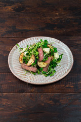 Green salad with steak, aubergine, sunflower sprouds and feta chese in ceramic plate on wooden background