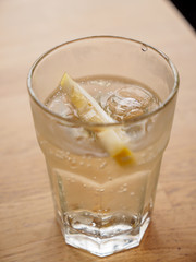 Closeup macro detail of an ice-cold glass of soda with a lemon wedge on a wooden table at a seaside cafe. Vertical orientation, shallow focus. St. Ives, England. Travel and drinks.