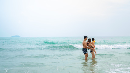 Happy asian family - father, mother, baby daughter hold hands and run with fun along edge of sea on sand beach. Active parents and people outdoor activity on tropical summer vacations with children.