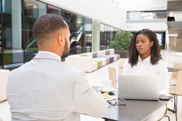 Young businesspeople having lunch break together. Business man and woman sitting at table in cafe, using laptop and talking. Lunch break or meeting concept