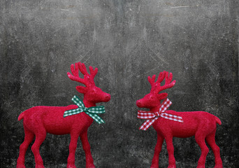 Zwei weihnachtliche Rentiere mit Schleife stehen vor dunkler Tafel mit Textfreiraum.
