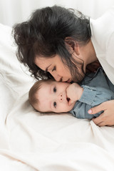 dark-haired mother kisses a one-year-old baby in a bright bed. Mom s love for her son