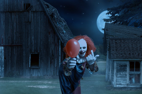 eerie clown with a balloon in hand in front of a scary scene