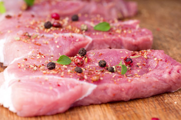 Raw pork steaks sprinkled with spices and herbs. Juicy raw steaks for a barbecue, close up.