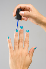 Sixth step by step of a french manicure. Painting the nail tips with a darker blue nail polish and letting it dry. On a grey neutral background.