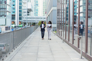 Professional businesswomen with folders on street. Multiethnic female business colleagues in formal wear holding folders, walking and talking outdoor. Coworkers concept