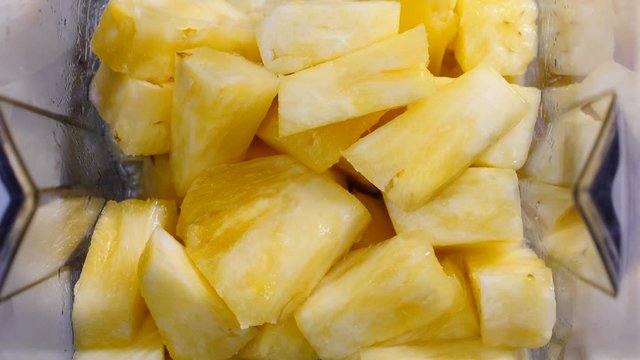 Making fresh fruits shake in blender. Pineapple ananas fruit slices being mixing in slow motion. Close up top view. Healthy food, dieting