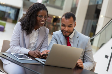 Cheerful business colleagues using laptop. Smiling young African American business people sitting at table and using digital devices. Technology concept