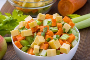 Vitamin salad of celery stalks, carrots, apples and cheese. Vegetable salad with cheese cut into cubes in a plate and a number of ingredients are.
