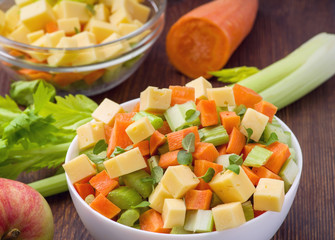 Vitamin salad of celery stalks, carrots, apples and cheese. Vegetable salad with cheese cut into cubes in a plate and a number of ingredients are.