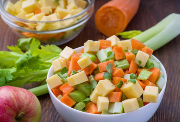 Vitamin salad of celery stalks, carrots, apples and cheese. Vegetable salad with cheese cut into cubes in a plate and a number of ingredients are.