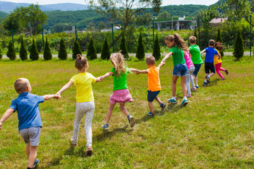 Children play holding hands on the green grass, back view