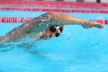 Swimming pool sport man doing crawl swim. Male swimmer with goggles and cap training in stadium for exercise. Cardio workout.