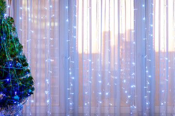 Christmas tree and garland on the background of the window, illuminated by the dawn