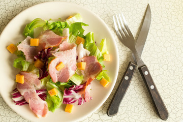 A plate of salad of green leaves, ham and cheese. Cutlery and a plate of fresh salad. Lunch. Intercontinental breakfast at the hotel.