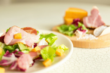 A plate of salad of green leaves, ham and cheese. Plate of salad with green leaves, ham and cheese. Fresh lettuce, cheese, ham and sea salt on a cutting board. Intercontinental breakfast at the hotel.