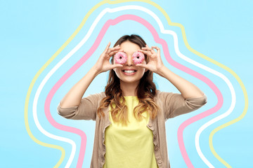 people, fast food and fun concept - happy asian young woman with donuts instead of eyes over blue background with glowing lines