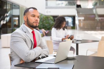 Pensive business leader thinking over new plan over cup of coffee. Young black woman drinking coffee and using tablet in background. Digital communication concept